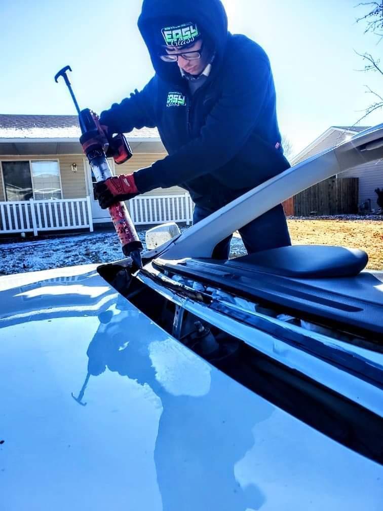Technician applies adhesive repairing windshield damage during mobile service, Grand Valley.